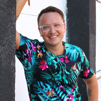 Liam Carnahan of Inkwell Content smiling at the camera in a colorful shirt while leaning against a wall